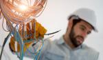 Electrical worker shown wearing a helmet and working on wiring.